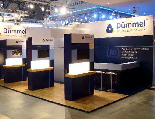 Beleuchteter Messestand mit dunkelblauen Wänden und Produktvitrinen, gebaut von Huber & Partner